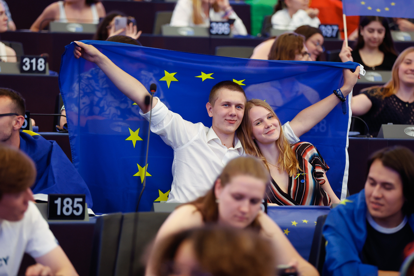 Tineri participanți la European Youth Event ținând steagul Uniunii Europene în plenul Parlamentului European